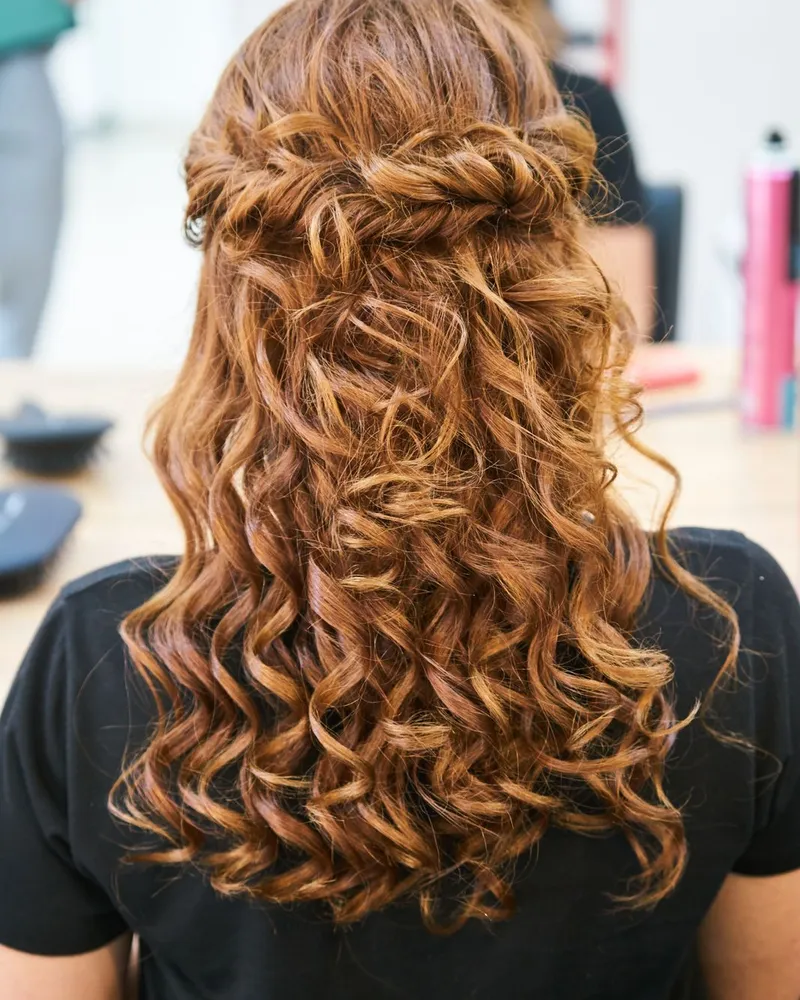 Vue de dos d’une coiffure terminée : longs cheveux bouclés châtain cuivré, avec un demi-attaché torsadé