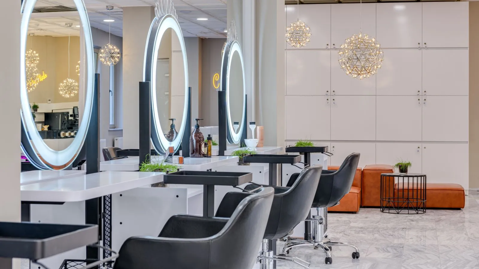 L’intérieur du salon : postes de coiffage alignés avec miroirs ronds lumineux, fauteuils noirs et banquette en cuir