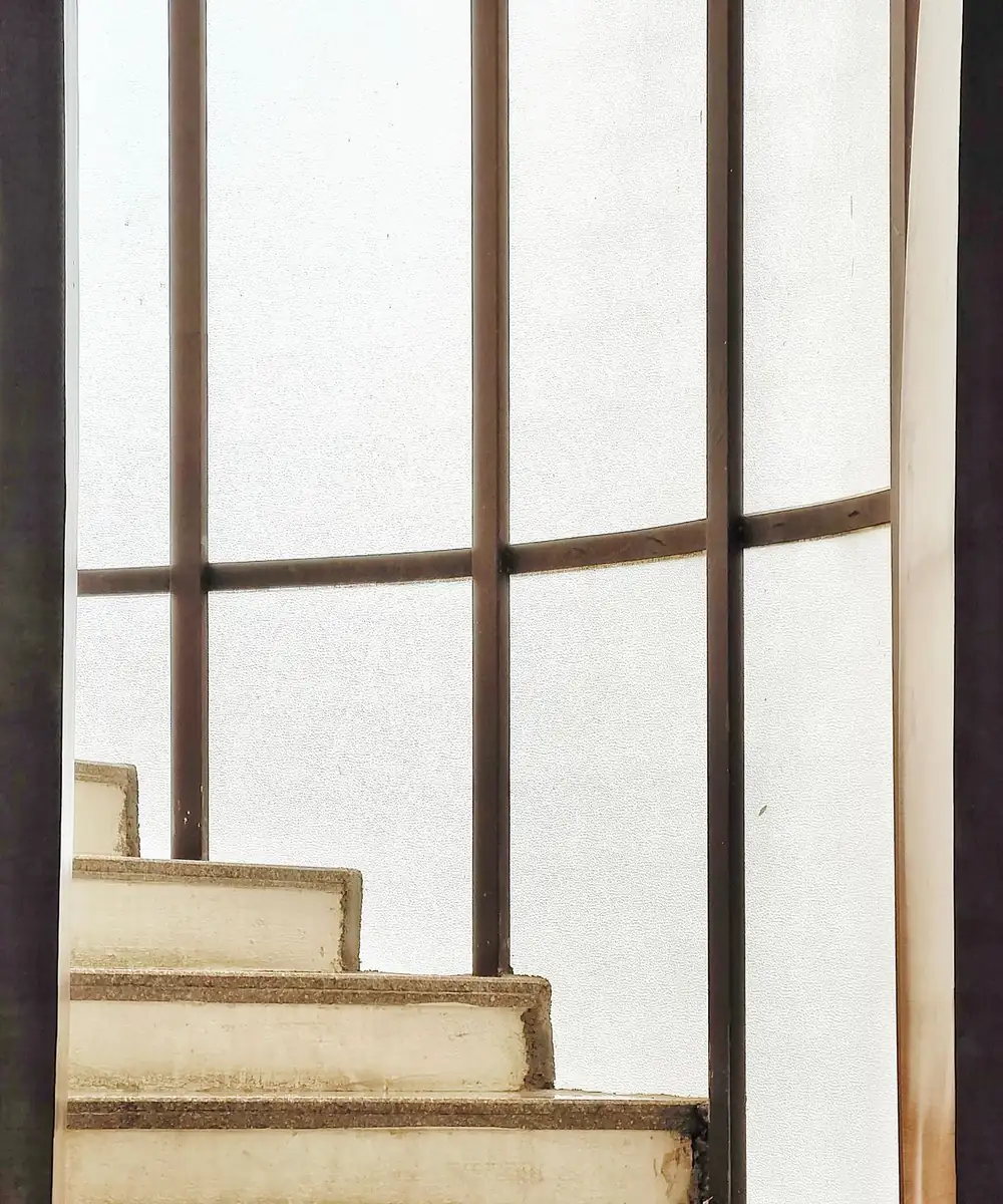 Escalier de pierre derrière une verrière d'acier à petits carreaux.
