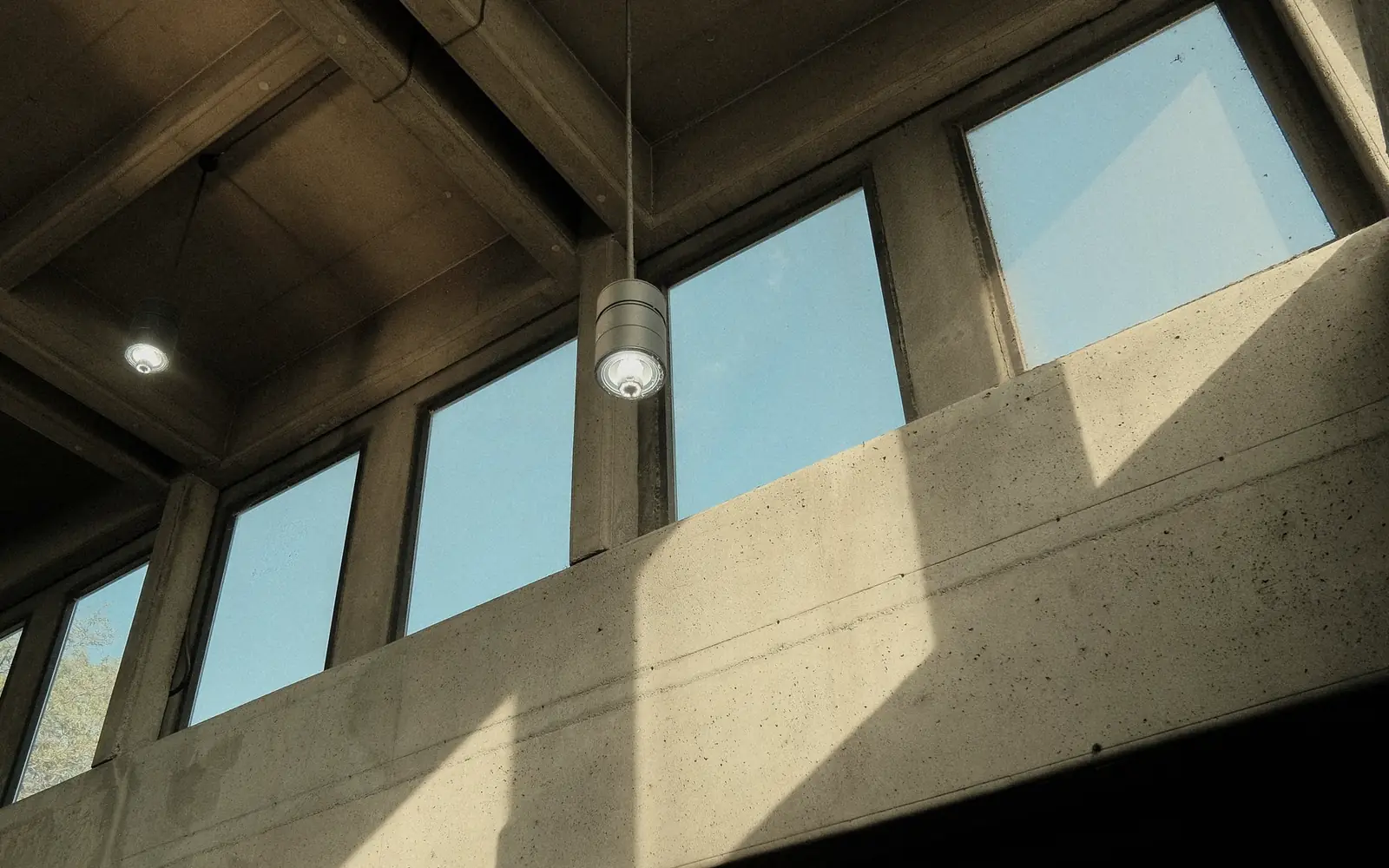 Nef couverte d'un plancher caisson en béton, éclairée par des fenêtres hautes ; lumière rasante sur un mur de refend.