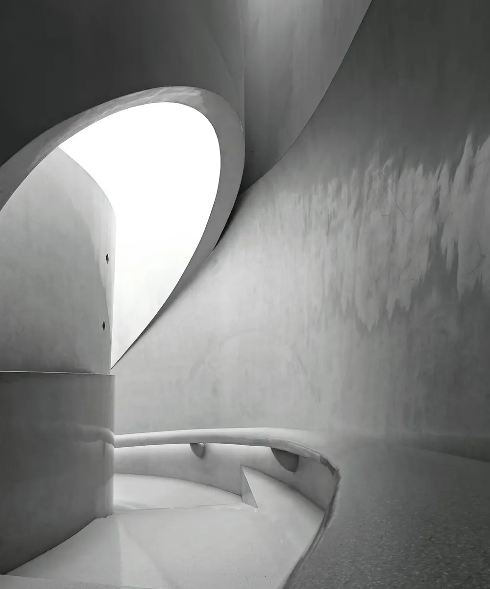 Volume circulaire en béton lissé percé d'un oculus ouvert sur le ciel, sol en terrazzo.