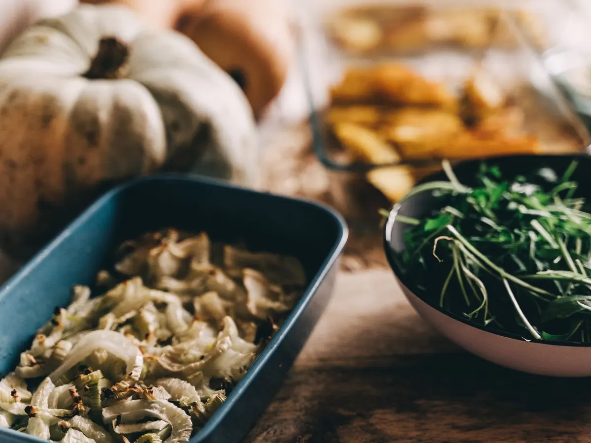 Plats de saison sur une table de bois : courge pâle, plat de fenouil rôti, saladier de roquette, légumes au four en arrière-plan.