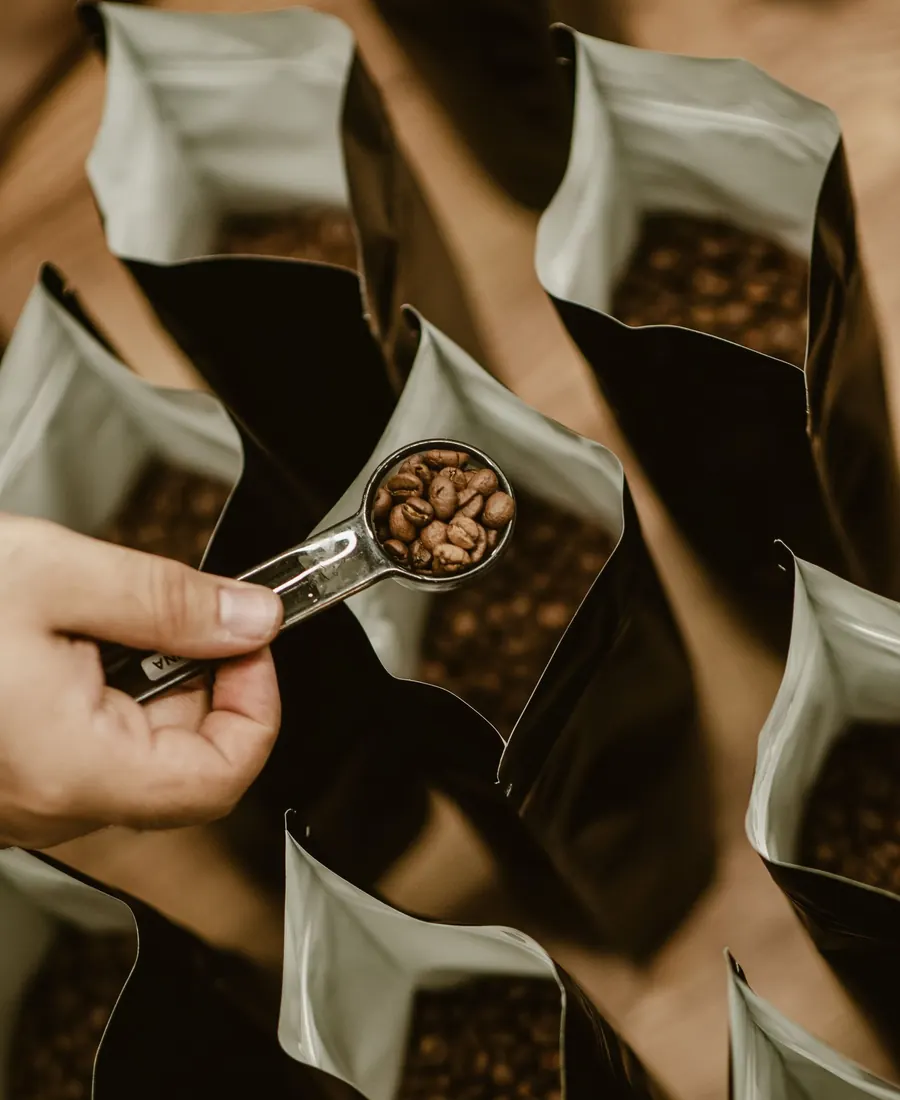 Une dosette de grains torréfiés tenue au-dessus de sachets de café ouverts