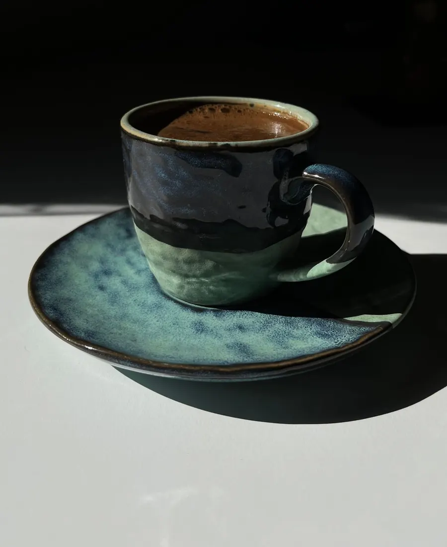 Une tasse en grès dans une lumière rasante, café noir encore fumant